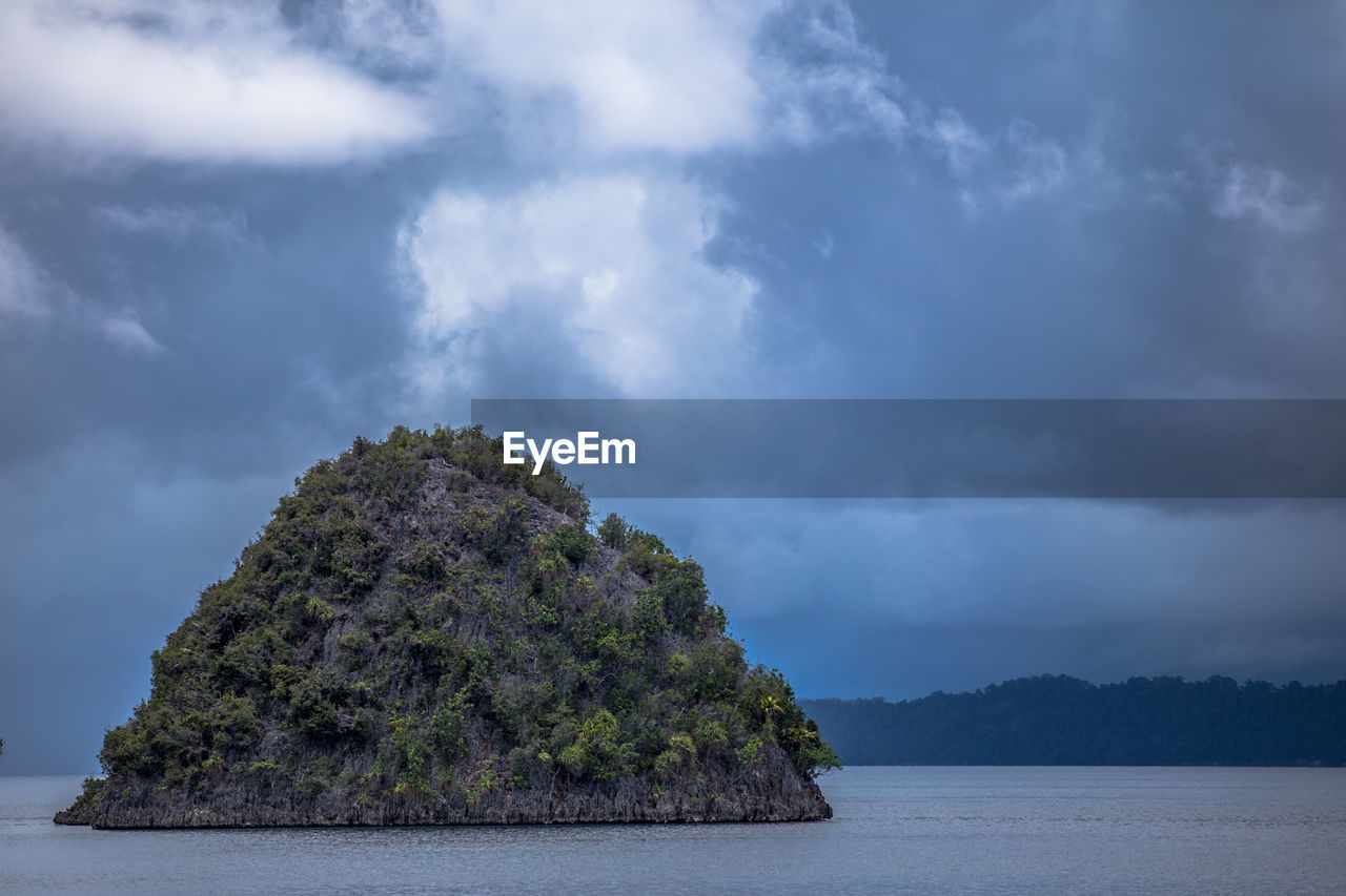 Rock formation in sea against cloudy sky at dusk