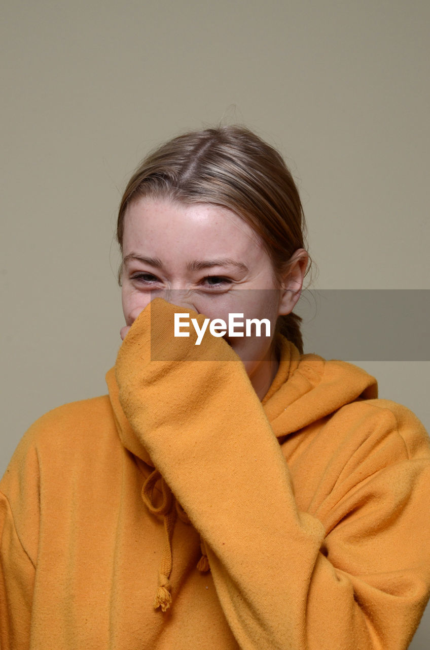 Portrait of smiling young woman against beige background