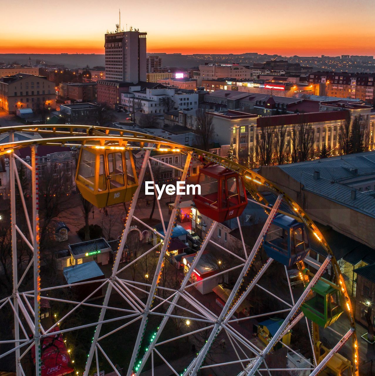 High angle view of illuminated ferris wheel against buildings in city during sunset