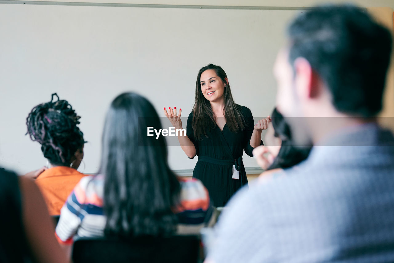 Happy teacher gesturing and explaining students in classroom