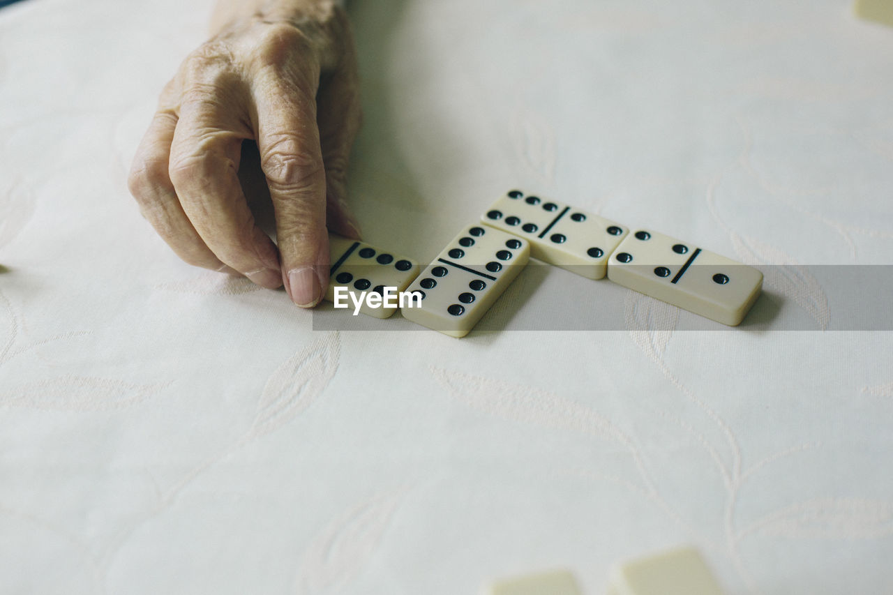 Cropped hand of person playing dominoes on white table