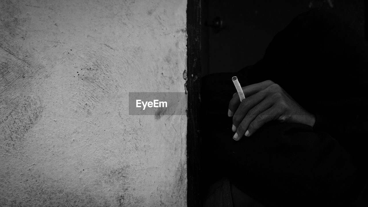 Midsection of man smoking cigarette against wall