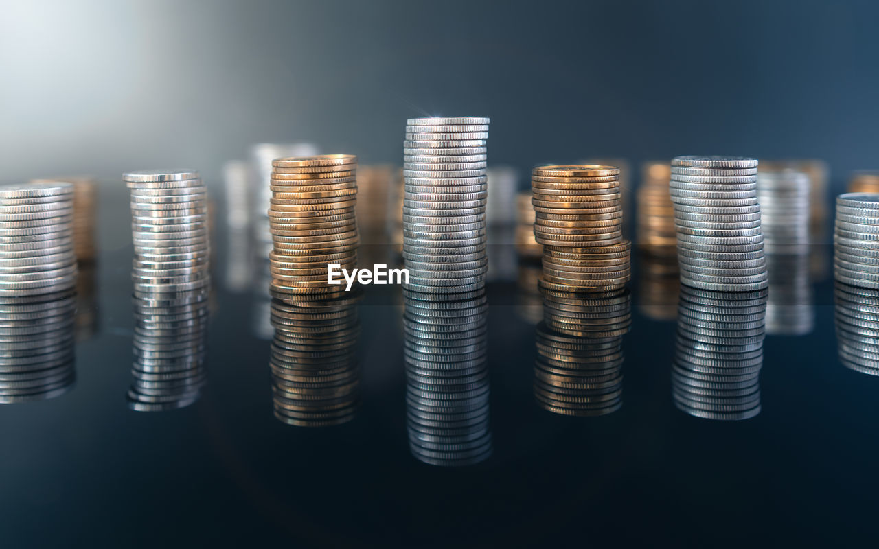 Piles of coins on a black, reflective surface seen from the top. inflation consuming our savings. 
