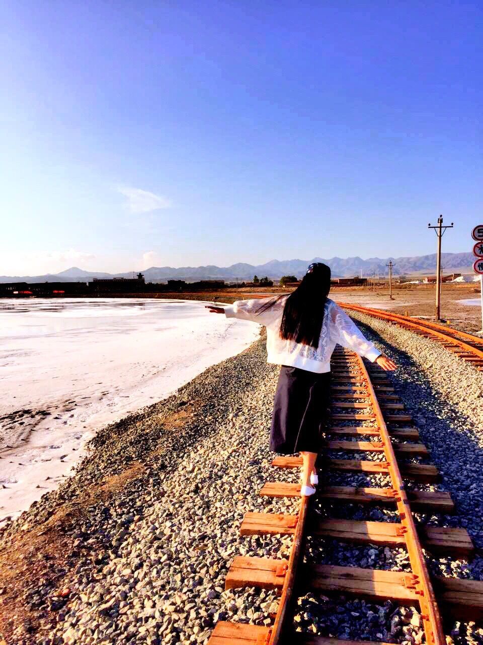 Rear view of woman with arms outstretched walking on railroad track