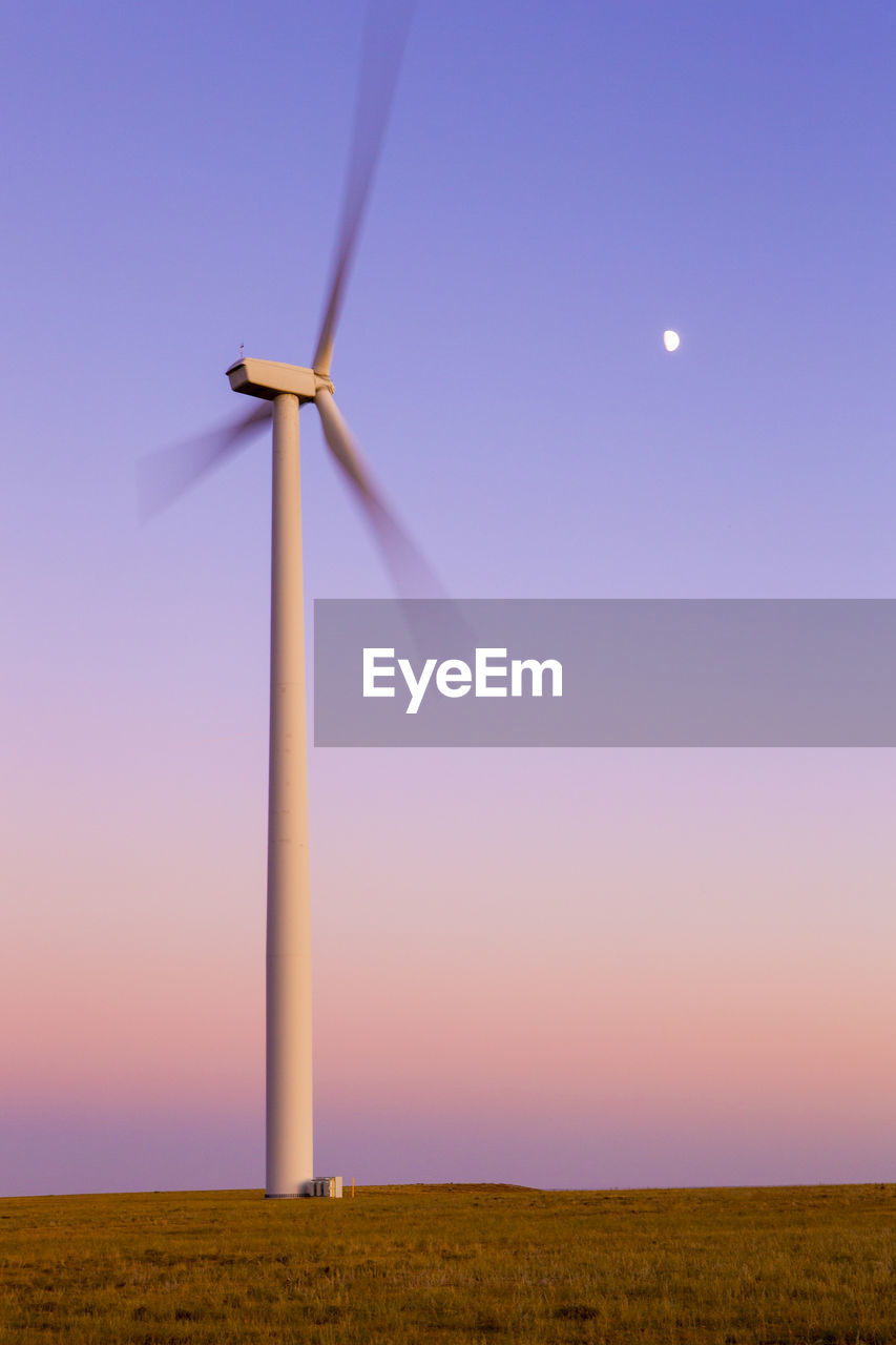 Wind turbine in motion against blue sky with moon