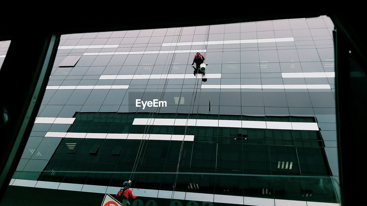Low angle view of people working on glass building