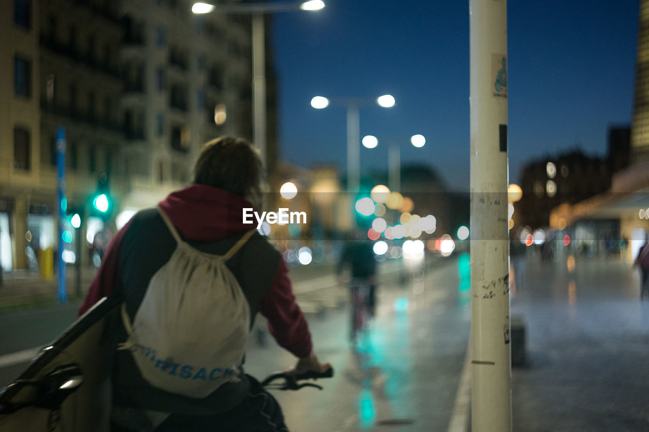 REAR VIEW OF MAN STANDING ON STREET AT NIGHT