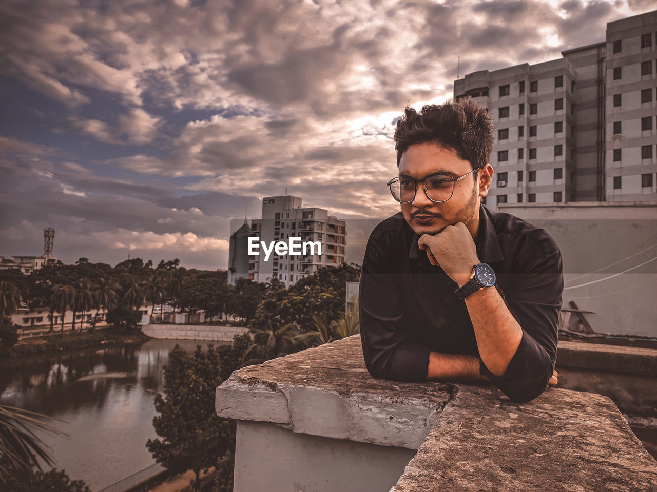 Young man sitting in city against sky