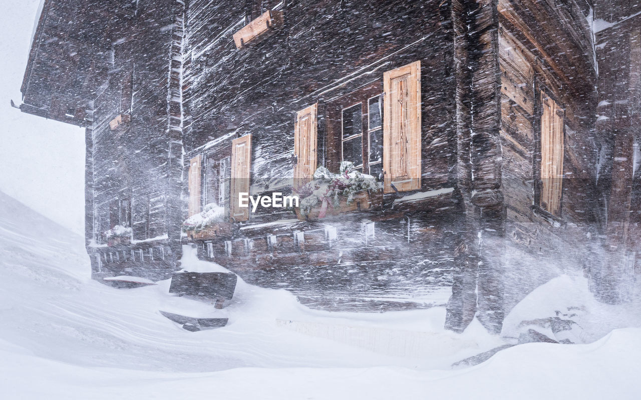 Low angle view of wooden cottage during snow storm