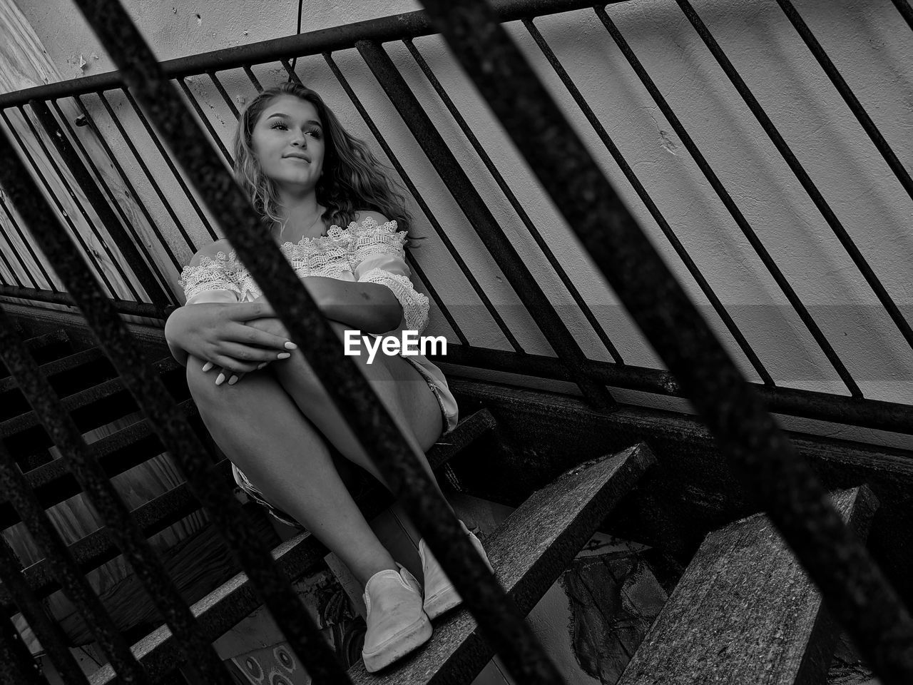 LOW ANGLE PORTRAIT OF WOMAN SITTING ON RAILING