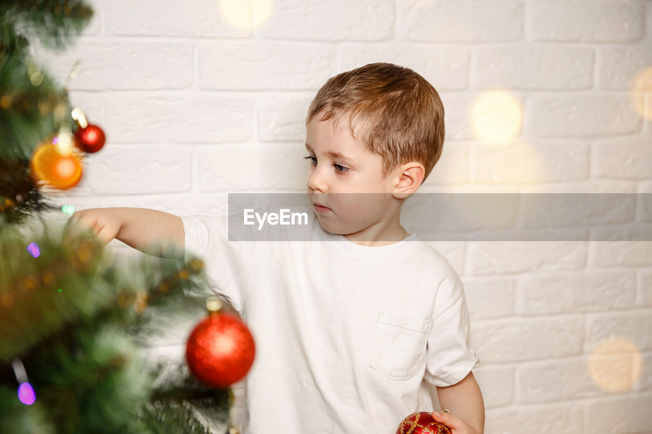 Cute boy decorating christmas tree against wall