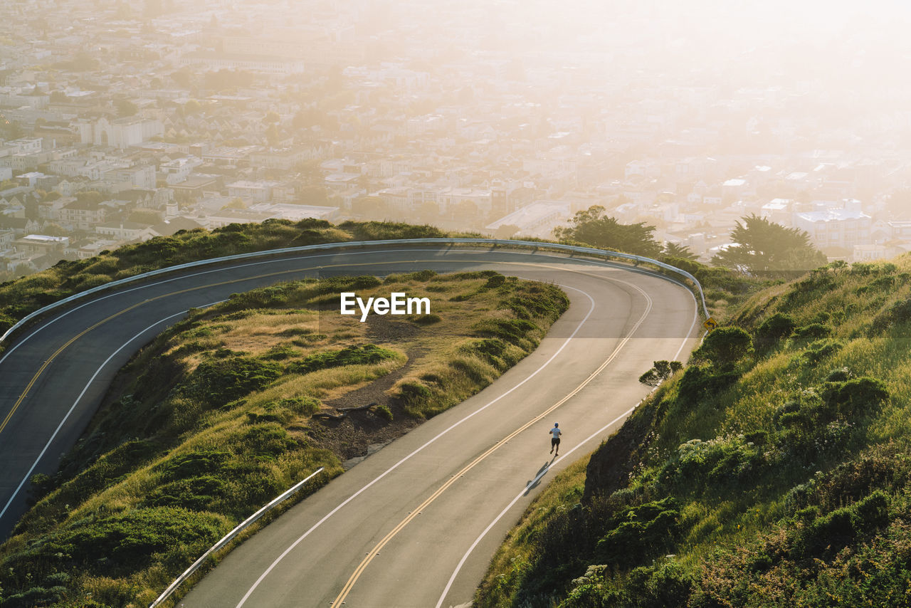 Aerial view of winding road on mountain against cityscape during sunset