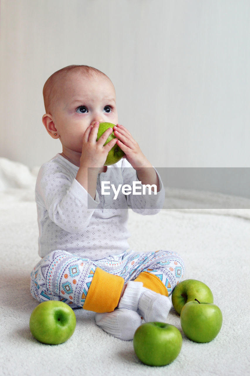 High angle view of cute baby girl sitting on carpet with apple at home