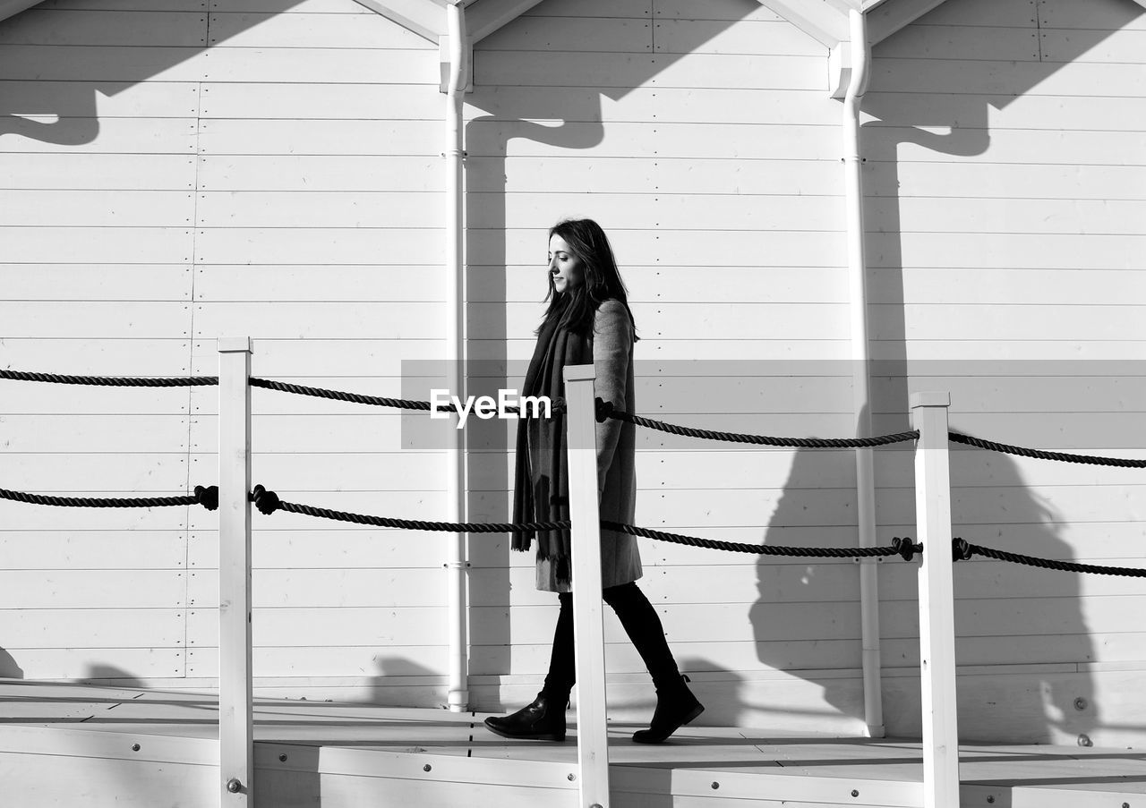 Side view of woman walking on sidewalk by building during sunny day