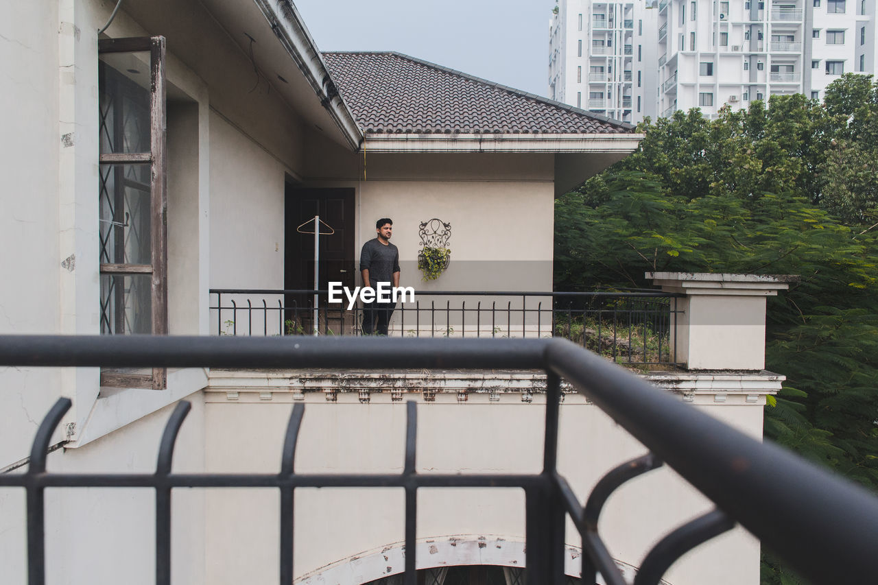 Portrait of a young adult against a built structure standing on his balcony