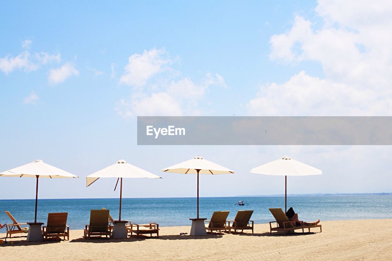 Lounge chairs and parasol on beach against cloudy sky