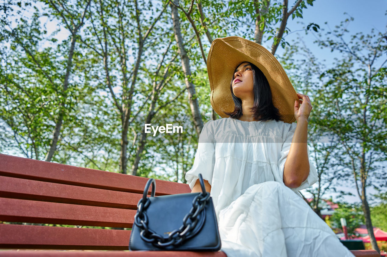 Young woman looking away while sitting on tree against plants