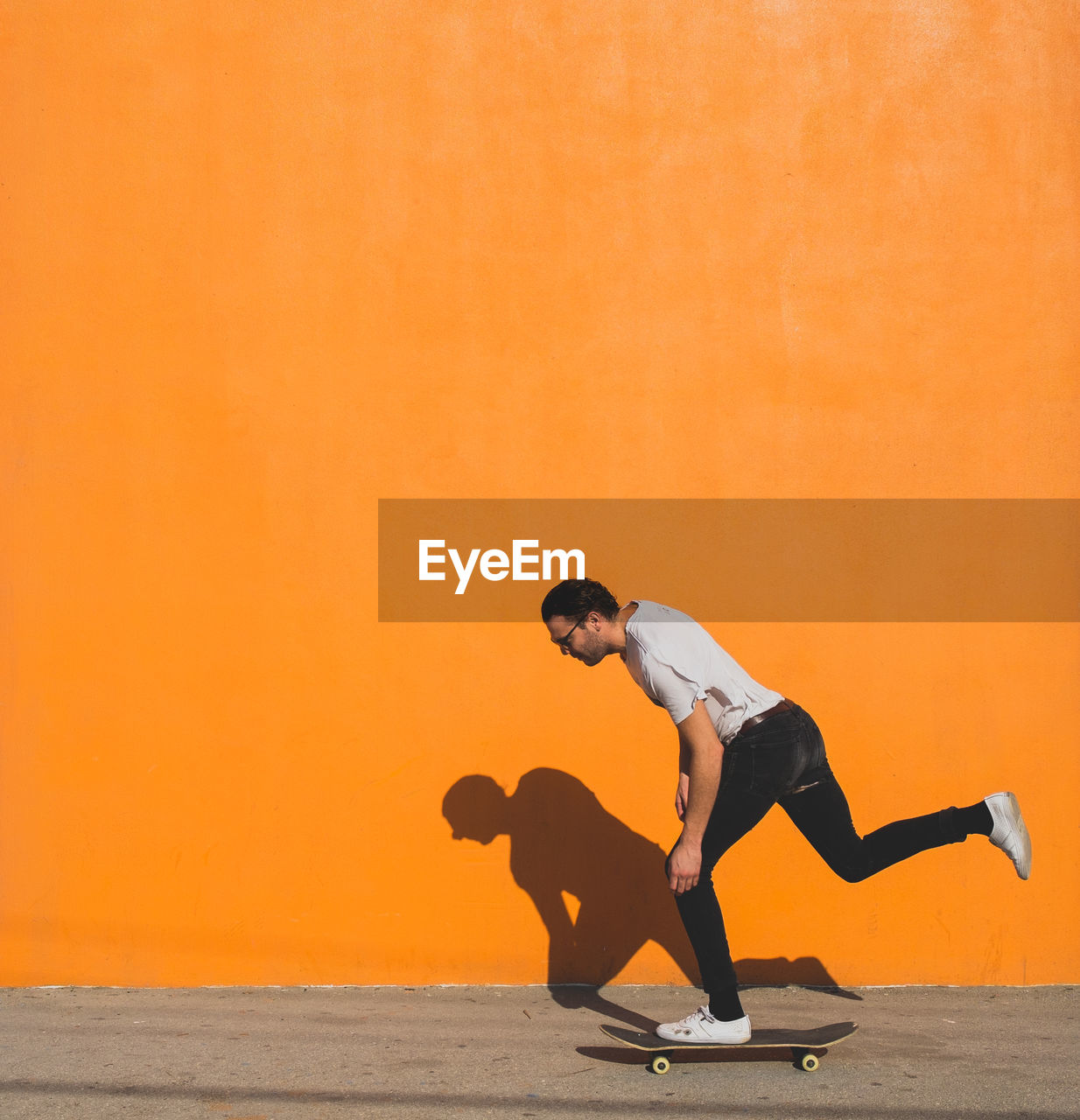 Man skateboarding on street against yellow wall