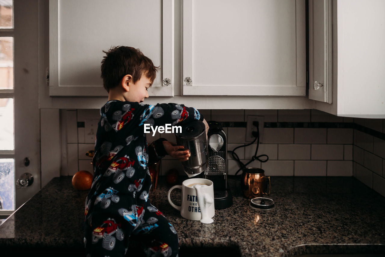 Young boy sitting on counter making coffee for dad