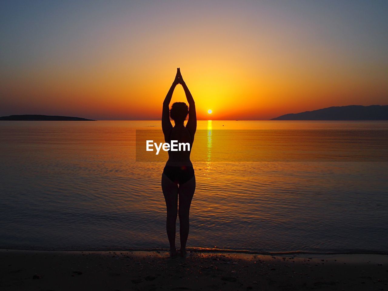 Silhouette woman doing yoga at beach during sunset