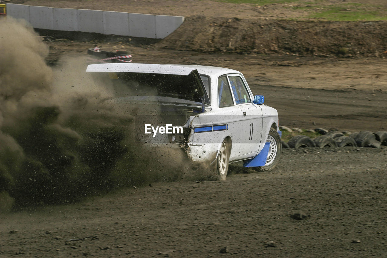 Rally car driving with a open trunk and a gravel dust behind him