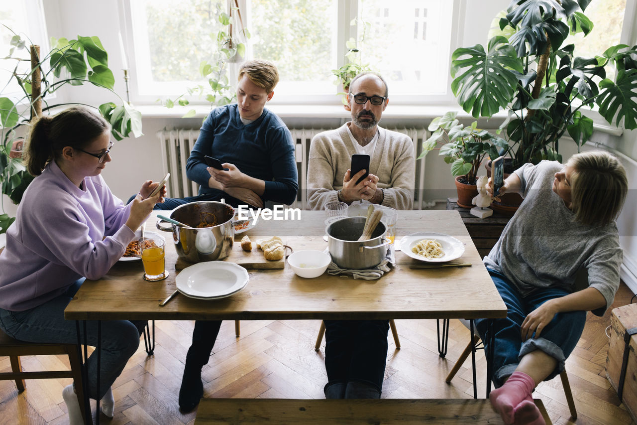 Family using smart phone while sitting on chair at dining table in home