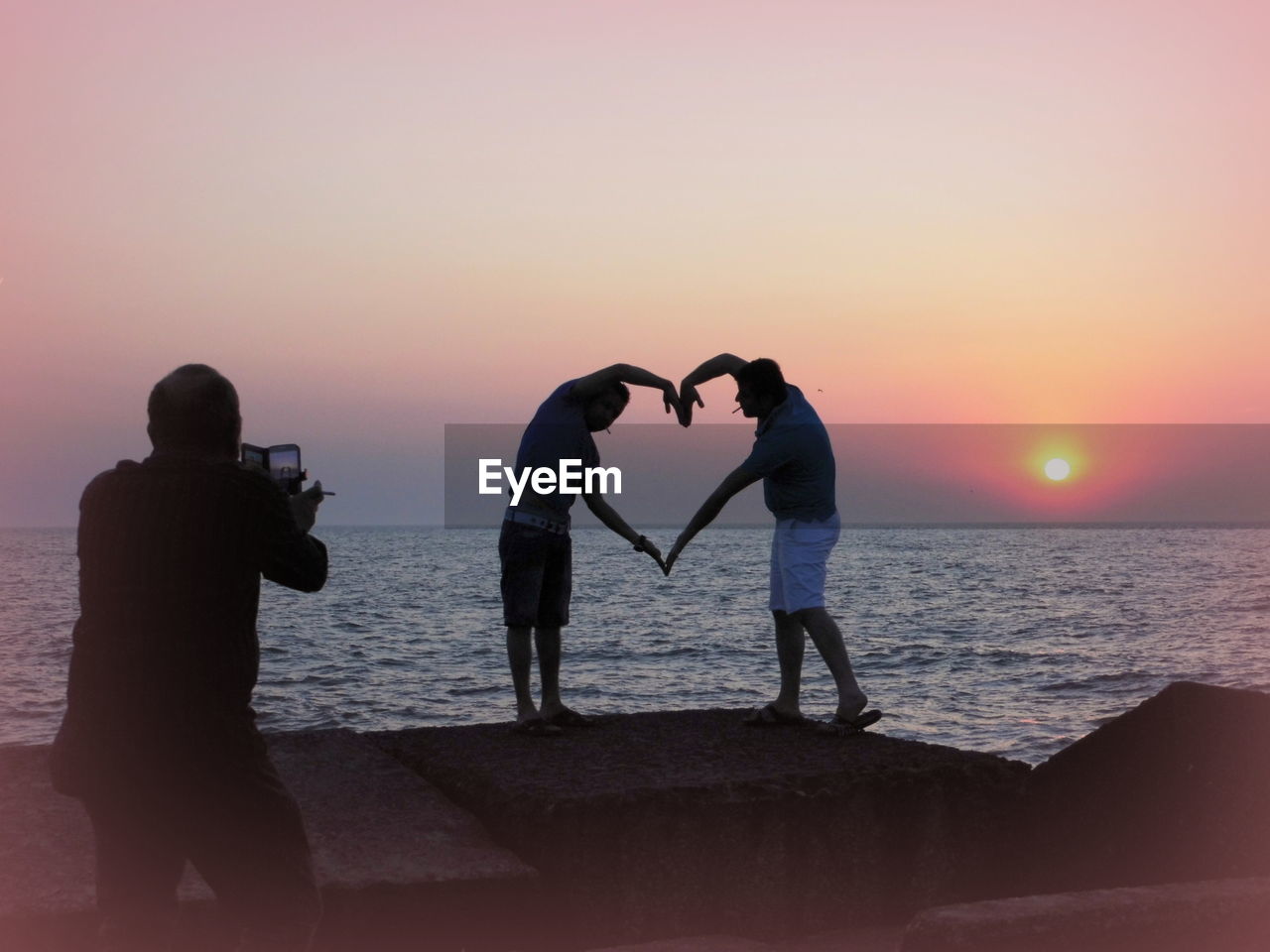 People forming heart of hand next to sunset against clear sky