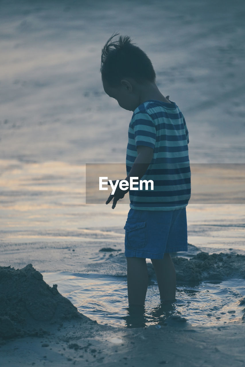 Boy standing on shore at beach against sky