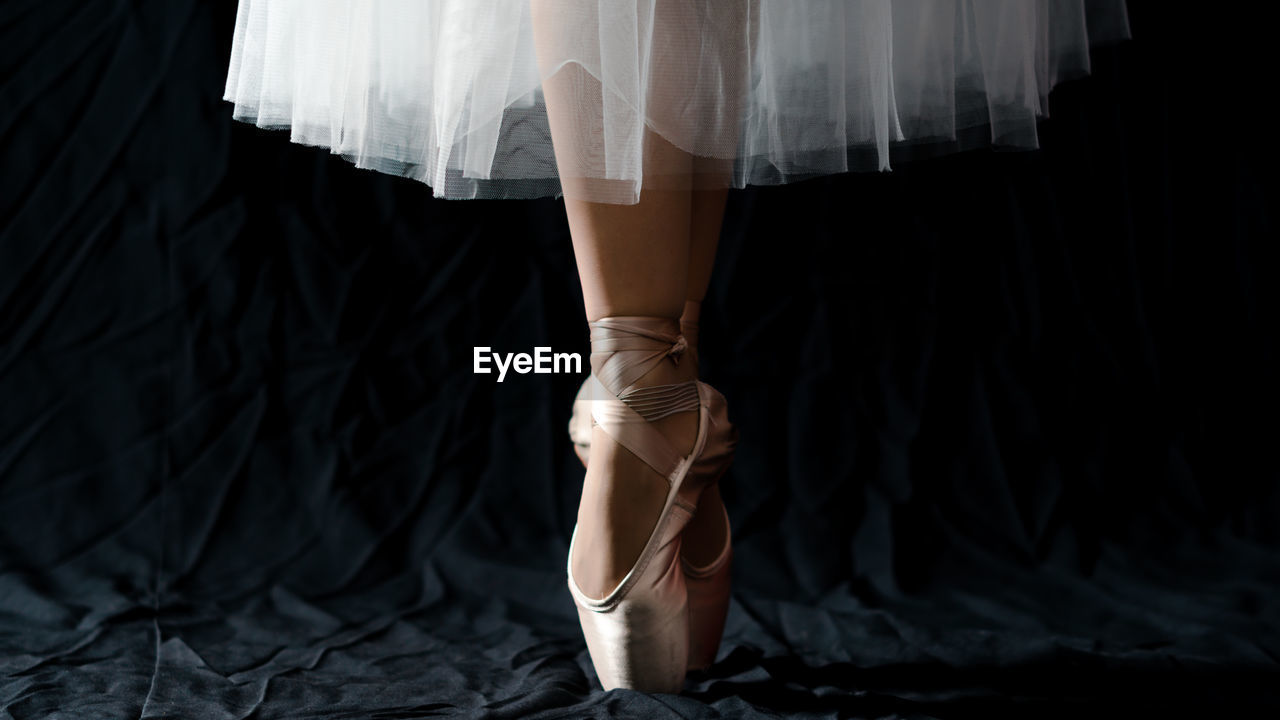 Low section of female ballet dancer dancing against black backdrop