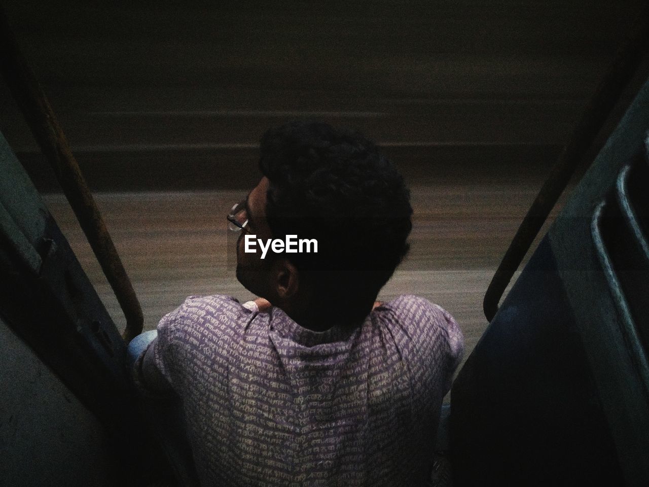 Rear view of man sitting on doorway in train at night