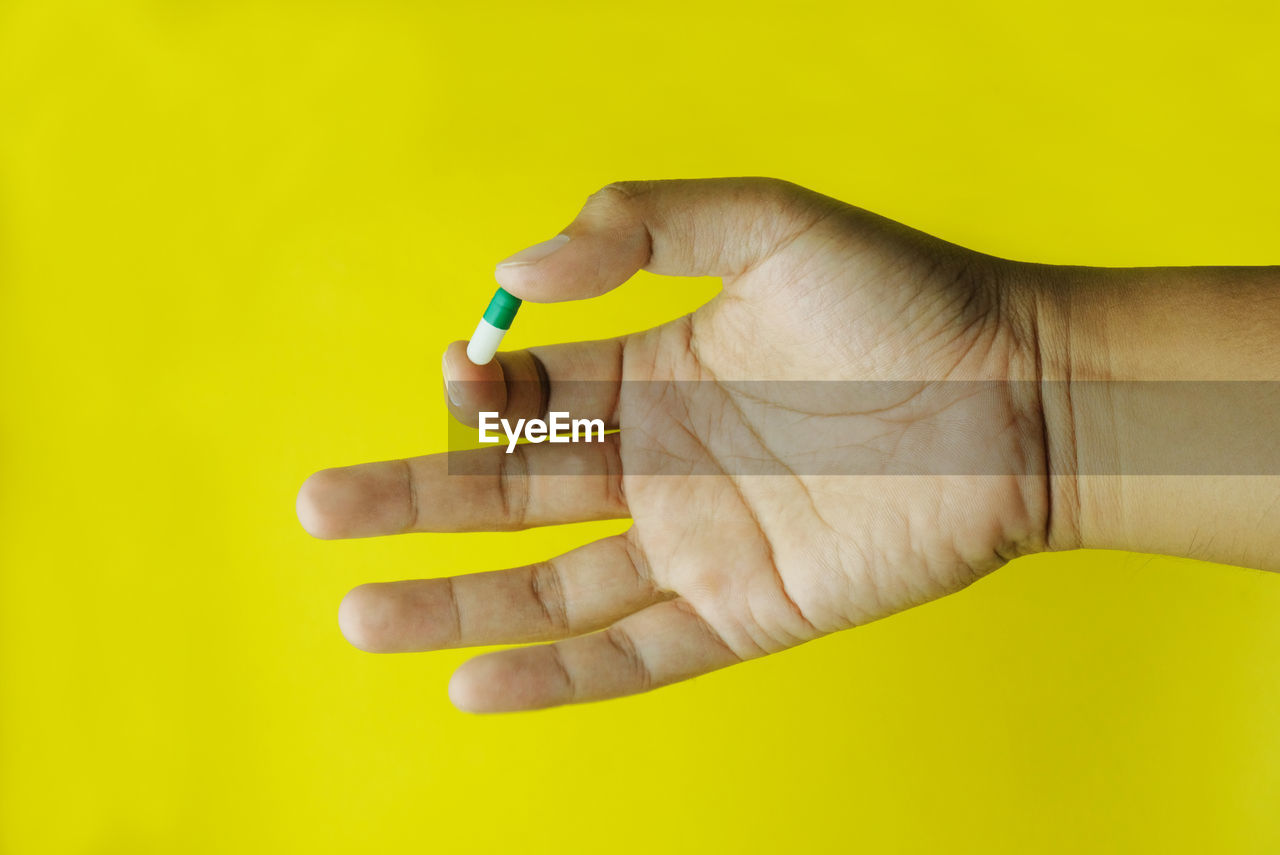 Hand hold pills isolated in yellow background