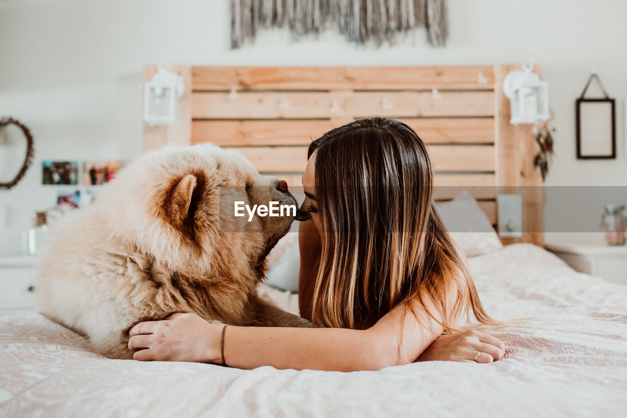 Smiling young woman lying with dog on bed at home