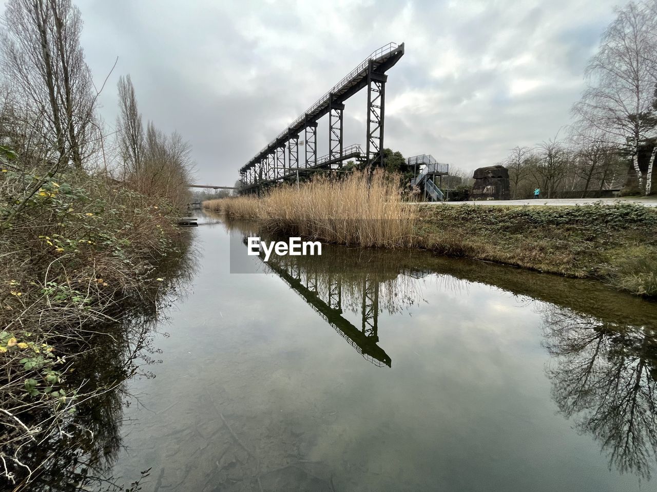 water, river, reflection, sky, waterway, bridge, cloud, nature, architecture, plant, built structure, tree, reservoir, environment, no people, tranquility, outdoors, landscape, beauty in nature, wetland, scenics - nature, day, social issues, overcast