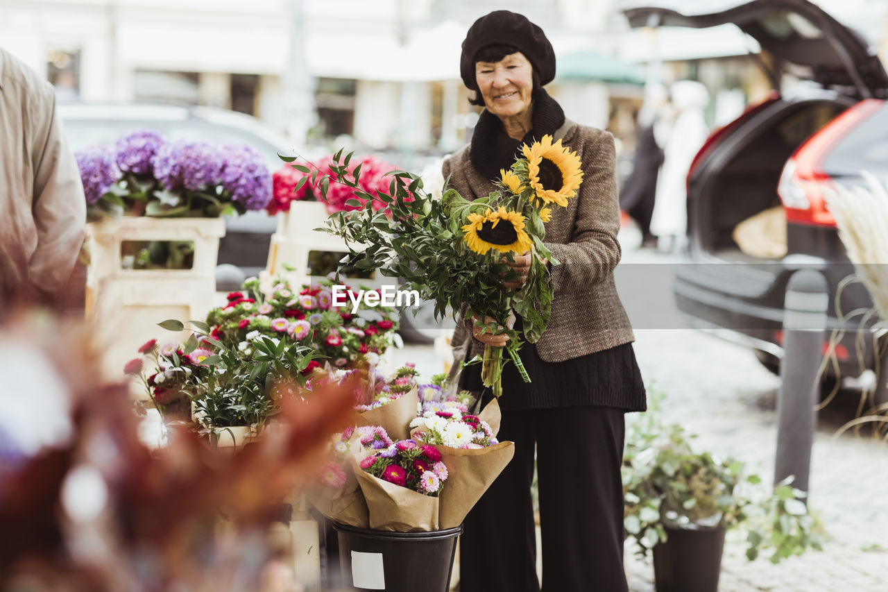 Smiling senior woman buying flowers from market