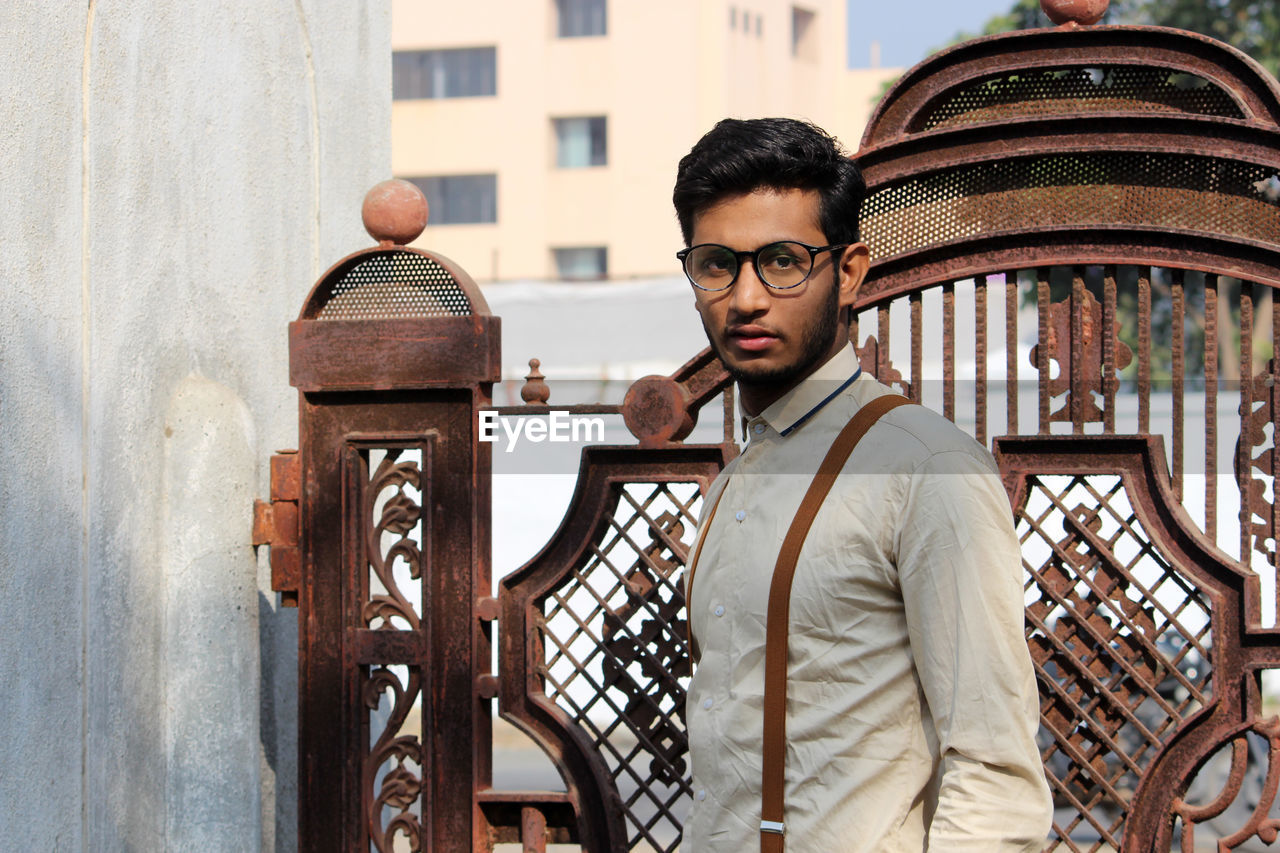 Portrait of young man standing against gate