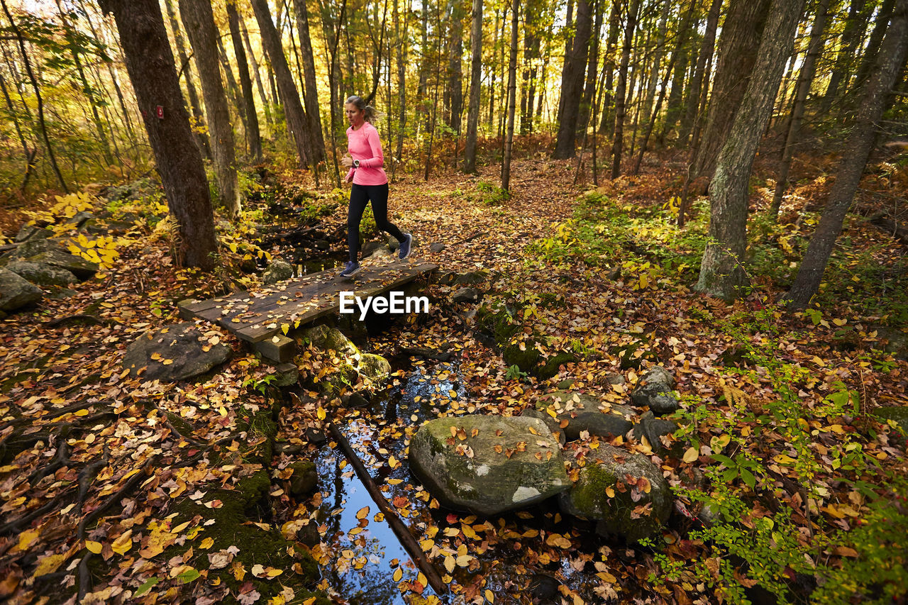 A woman running over a small trail bridge in the woods.