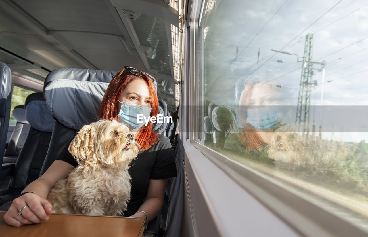 Young woman wearing mask sitting with dog in train