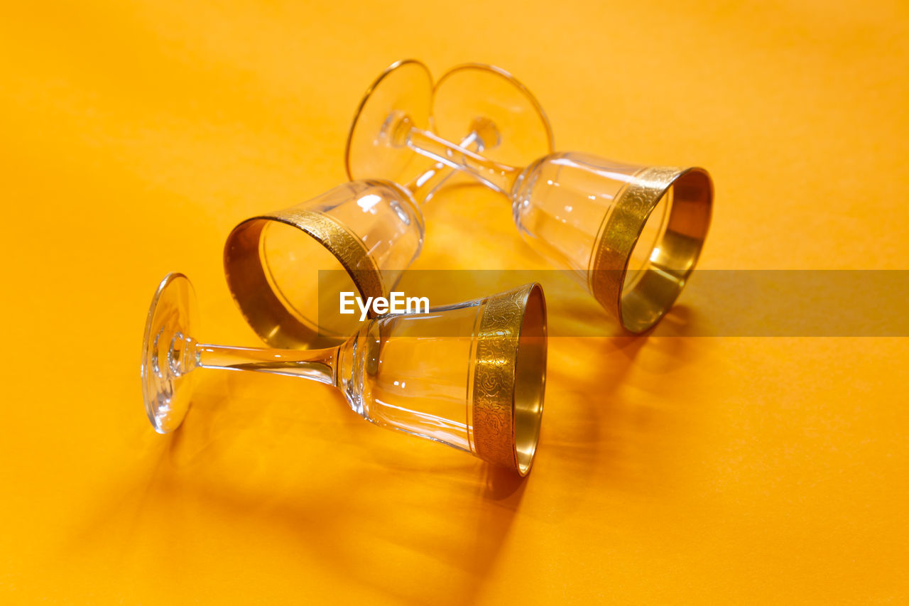 Closeup of three gold-rimmed liqueur glasses displayed lying down on bright orange background