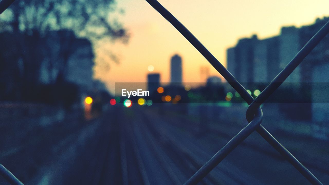 Railroad tracks during sunset seen through fence