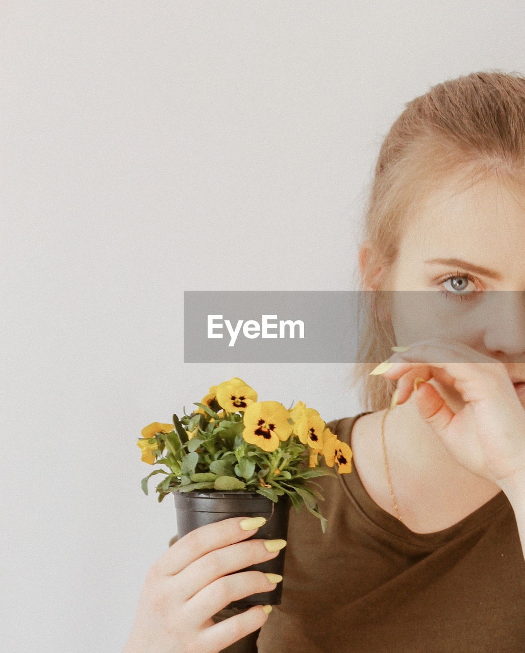 Portrait of young woman holding potted flowers against wall