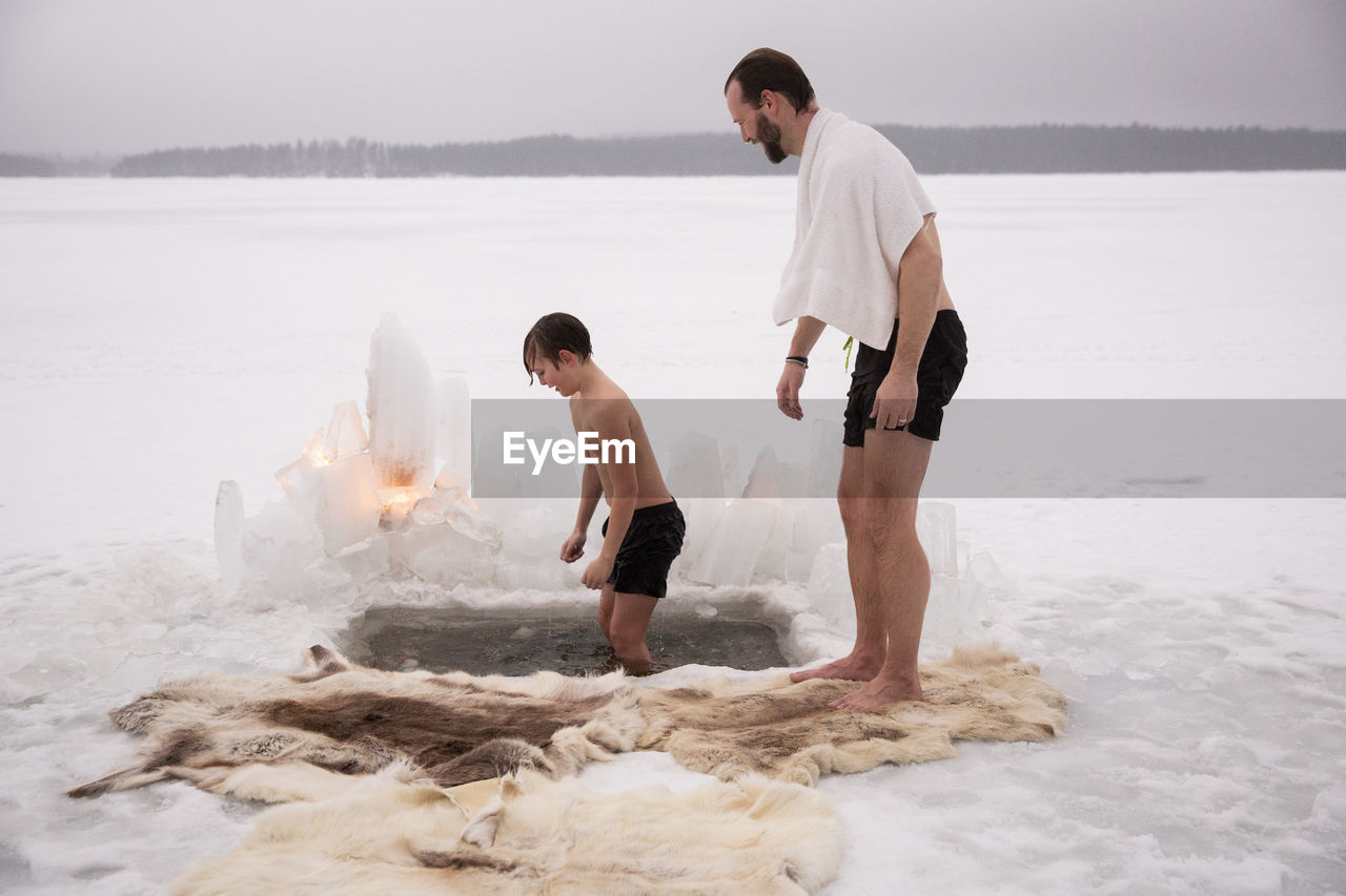 Side view of mature man looking at son taking ice bath at frozen lake