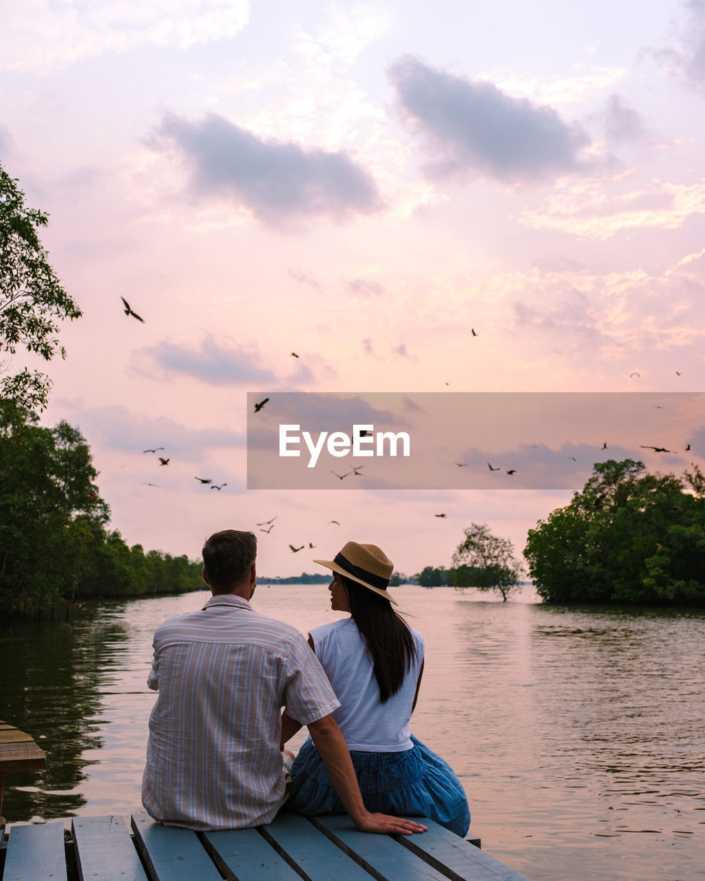 rear view of man sitting on boat on lake against sky during sunset