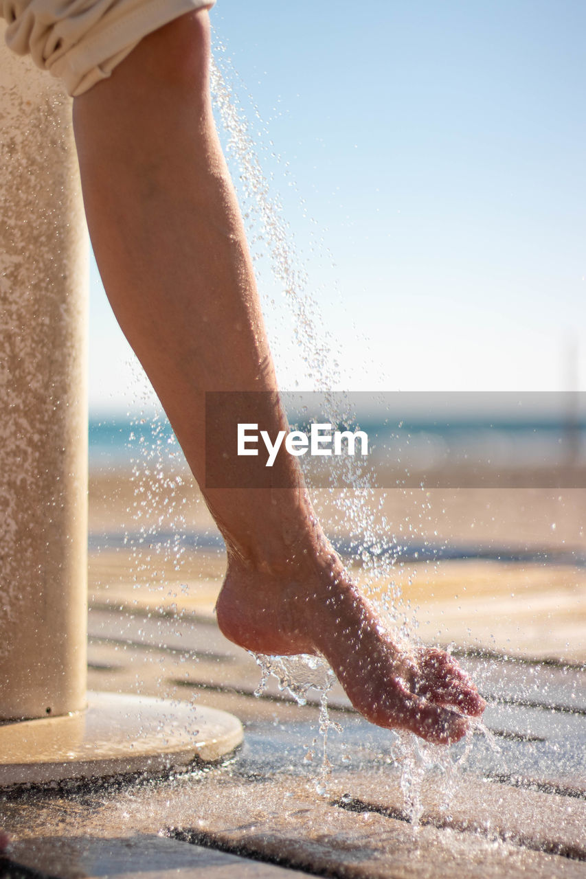 Woman wetting her feet with a shower to clean them from the sand after leaving the beach.