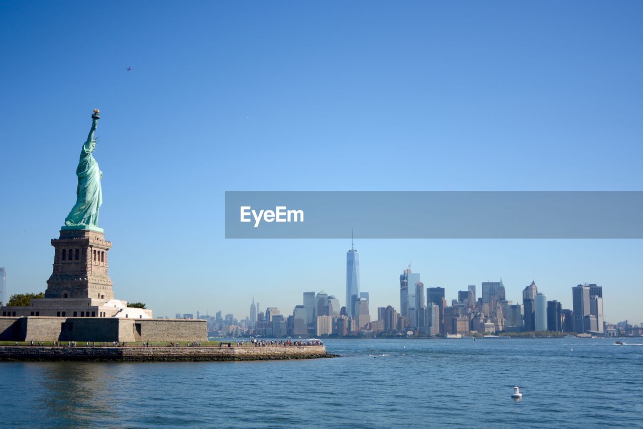 Statue of liberty by cityscape against clear sky