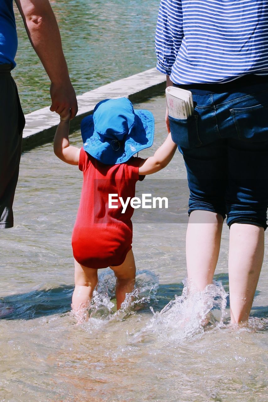 Midsection of parents with child wading in lake