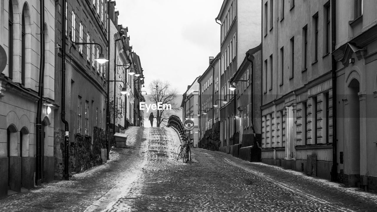 REAR VIEW OF WOMAN WALKING ON ROAD AMIDST BUILDINGS