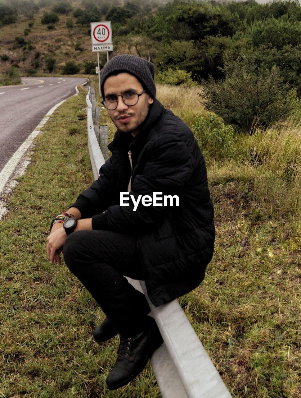 Portrait of young man sitting on railing at roadside