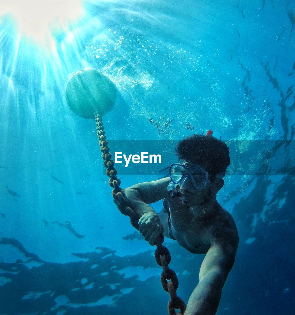 Low angle view of shirtless man holding chain in sea