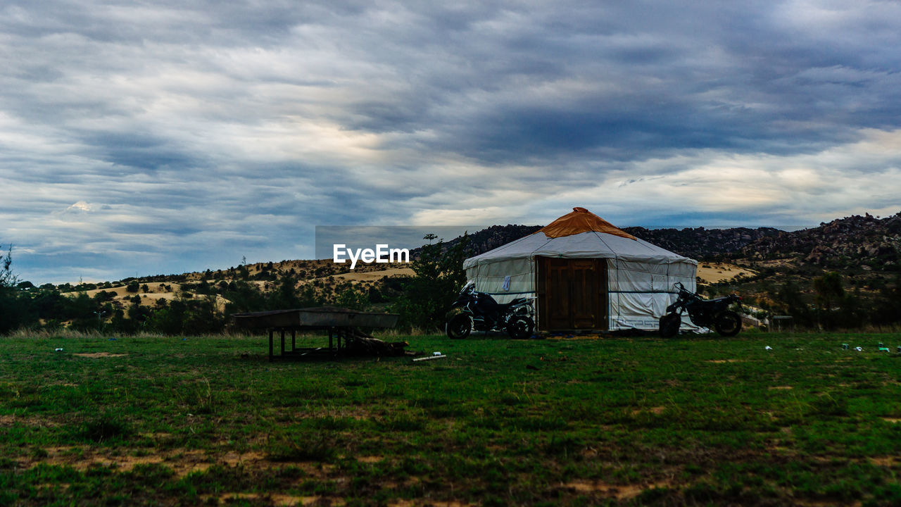 BUILT STRUCTURE ON FIELD BY HOUSES AGAINST SKY