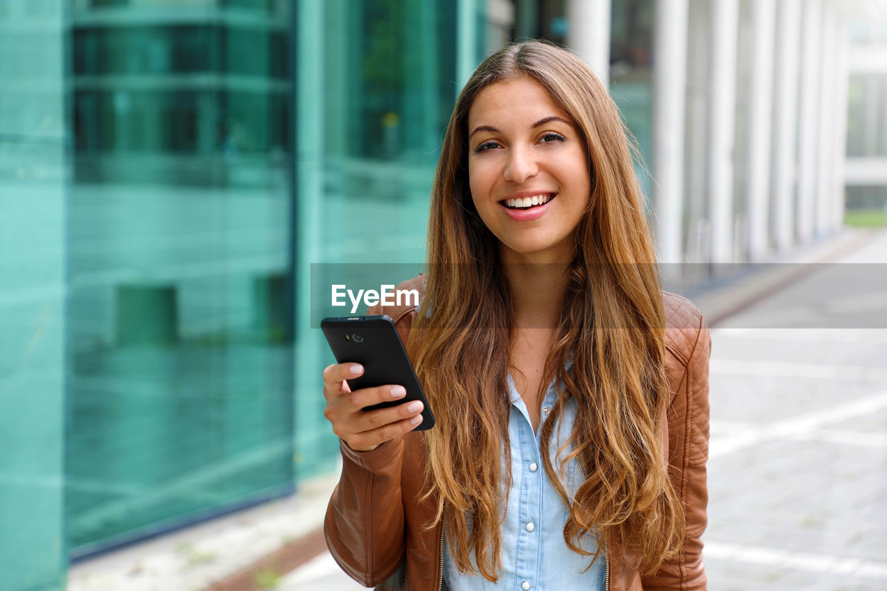 Smiling woman using smart phone while standing in city